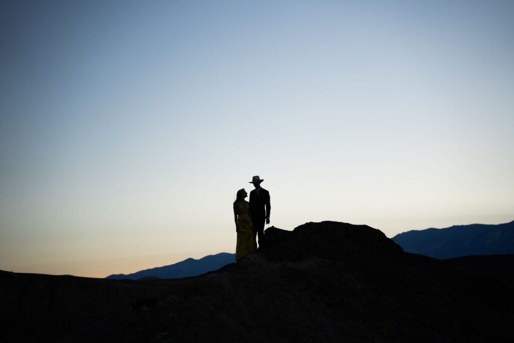 Silhouette of a couple standing on a hill as the sun sets behind them in Death Valley National Park