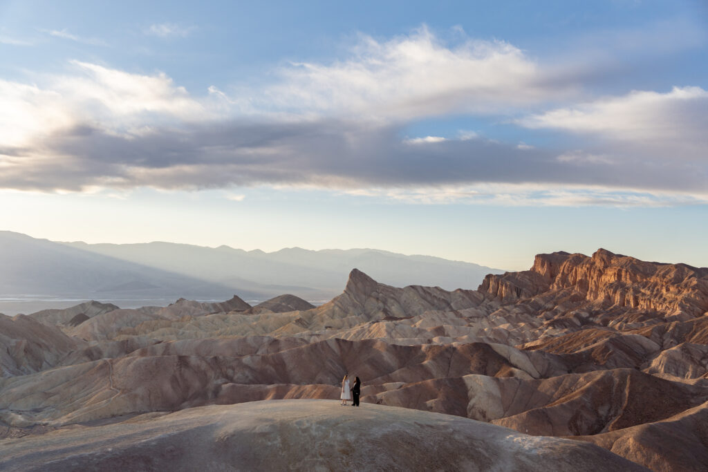 A couple holds hands amidst a dramatic desert landscape as the sun sets behind mountains on their elopement day