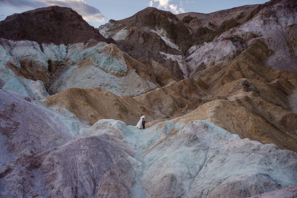 A couple hugs surrounded by colorful hills of purple, turquoise, and brown in Death Valley National Park