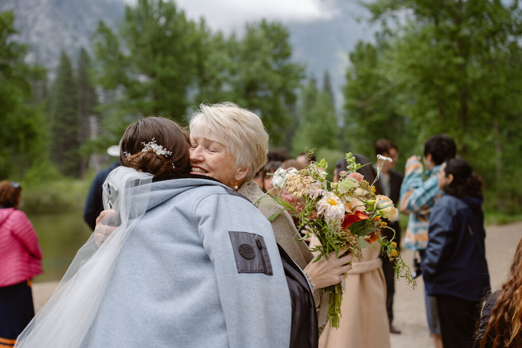 a grandmother embraces the bride wearing a jacket at their outdoor elopement ceremony