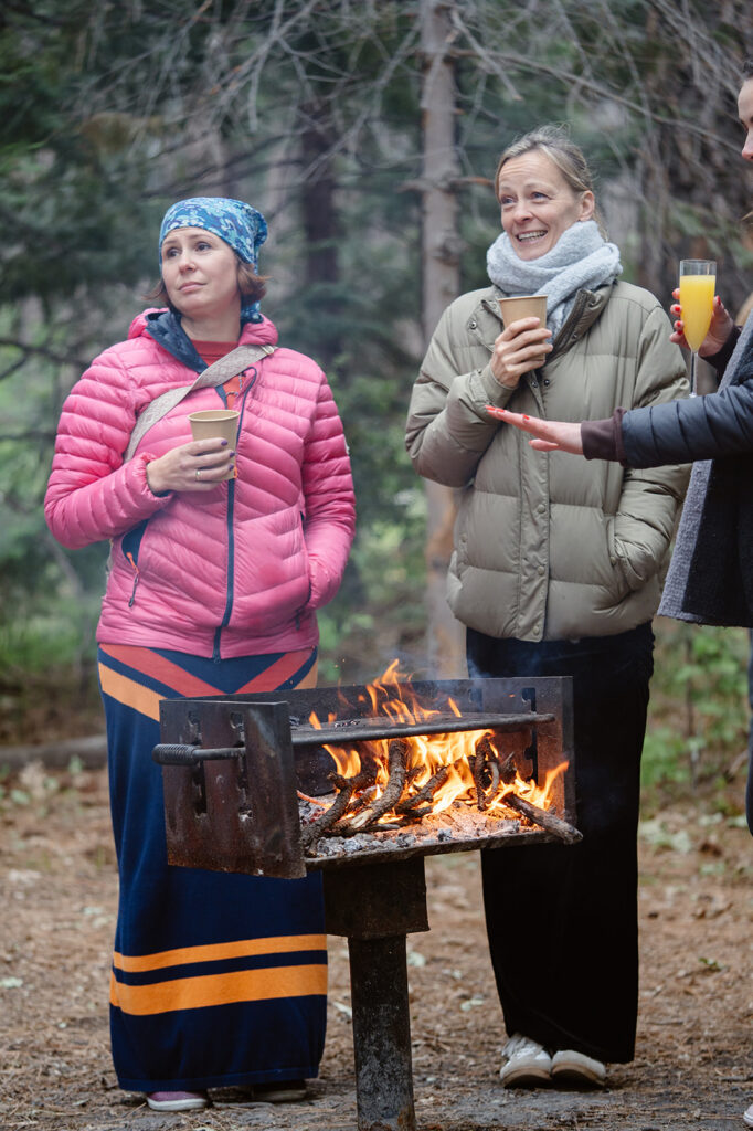 elopement guests bundled up in jackets and warming themselves near a fire