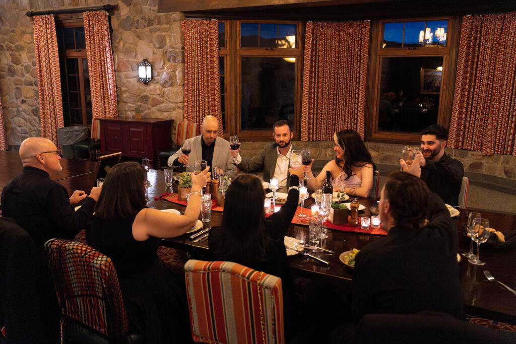 a newlywed couple and their guests cheers at dinner with raised glasses
