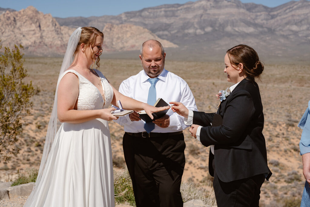 A woman puts a wedding band on another woman's finger at their queer elopement in red rock canyon