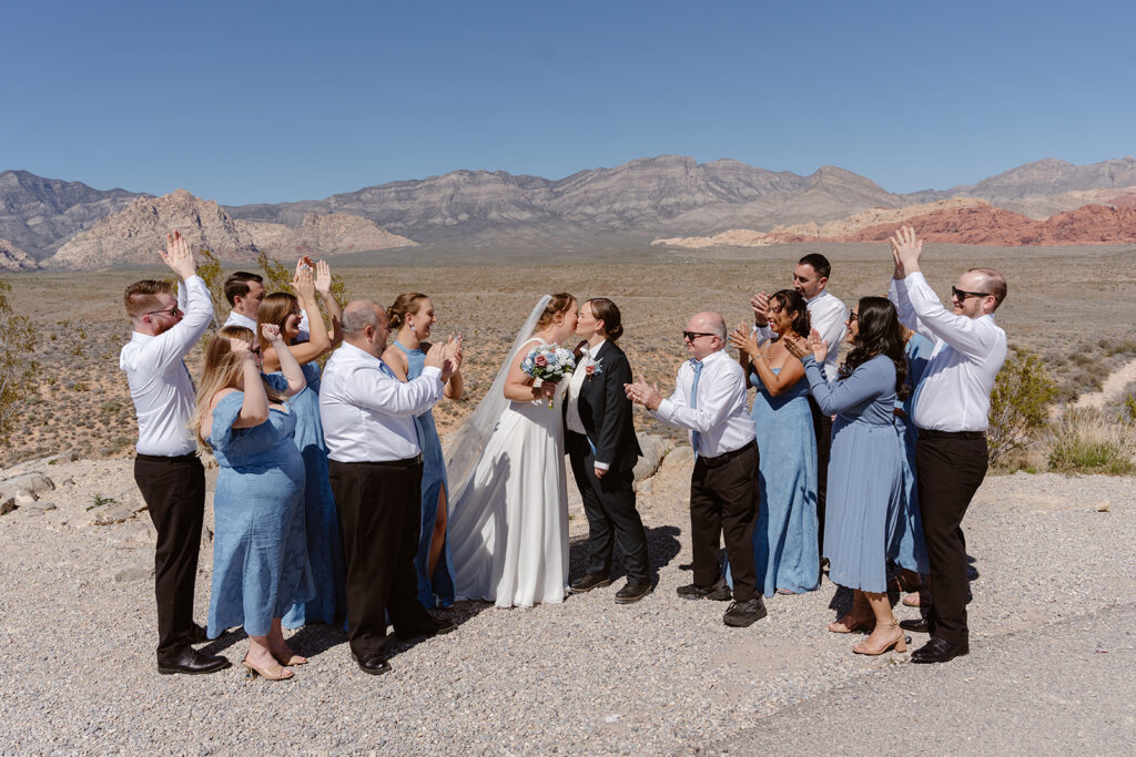 a queer couple kisses amidst cheering friends and family at their elopement ceremony