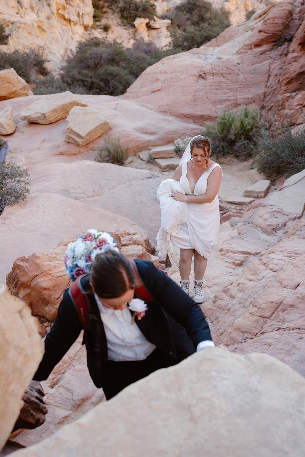Two brides hike in their wedding attire after their queer elopement in red rock canyon