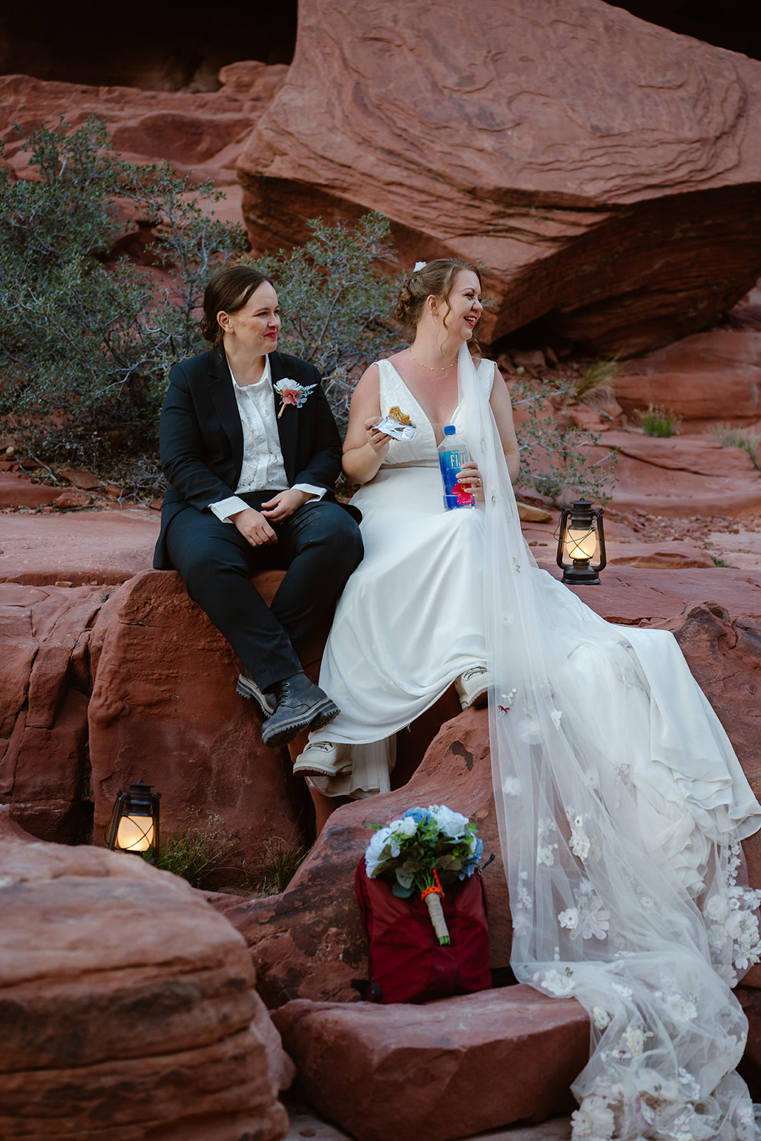 Two women eat snacks and laugh while sitting on red rocks