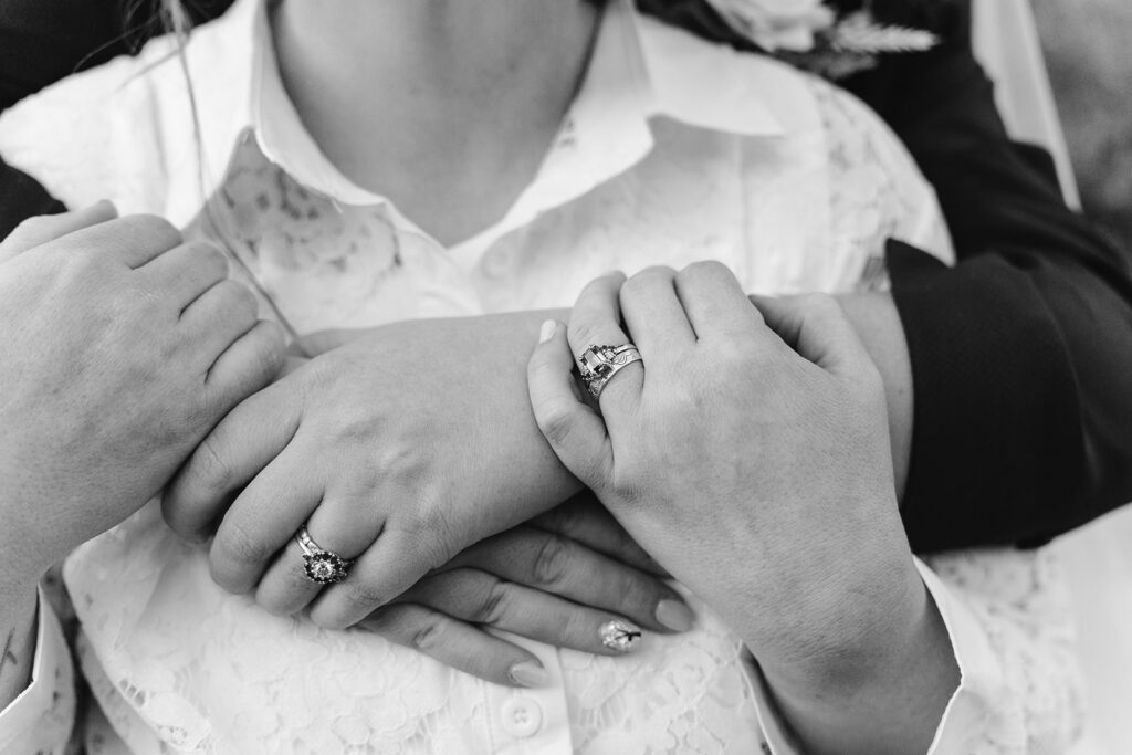 close up black and white image of arms wrapped around each other, both wedding rings featured prominently