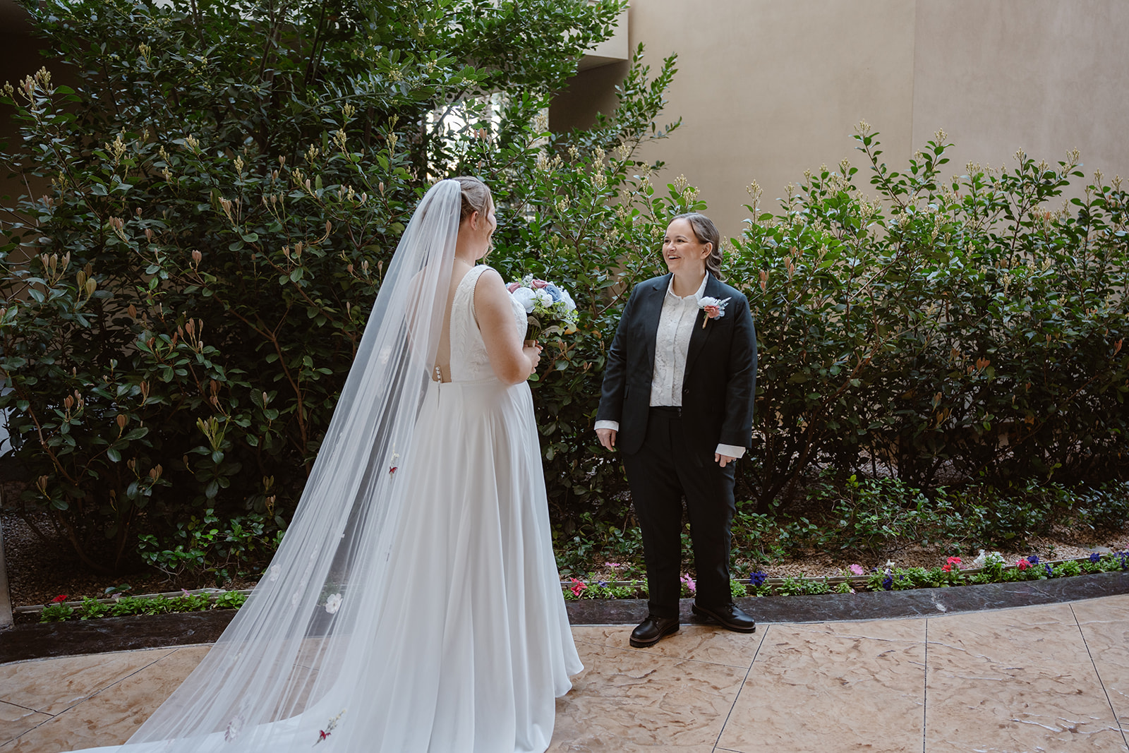 two brides share a first look. one is in a white wedding dress, the other in a navy suit