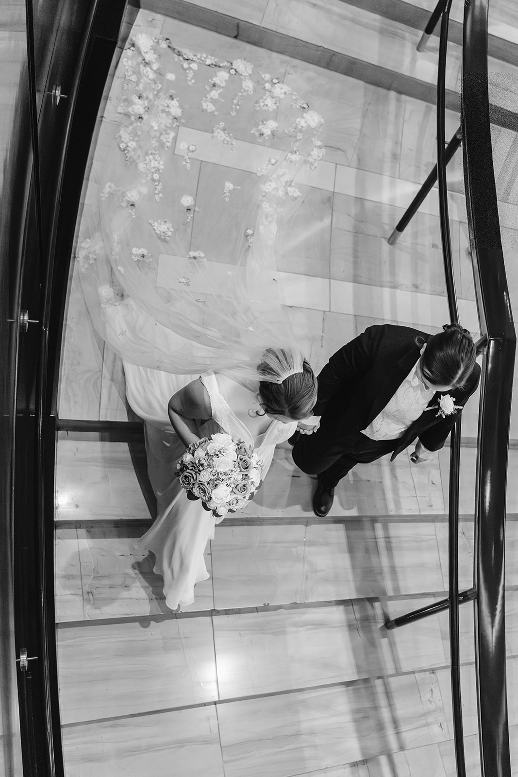 two brides walk hand in hand down a large marble staircase at the red rock resort