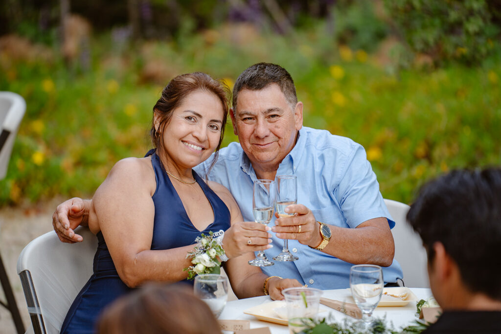 a couple holds up glasses of champagne and smiles at the camera