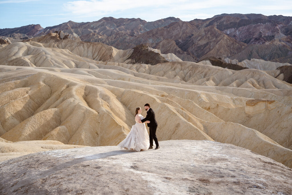 A bride and groom dance on tan colored hills at Zabriskie Point in Death Valley