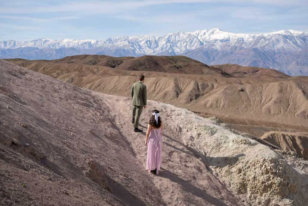 A couple stares at a row of snowy mountains in the distance