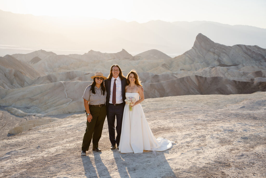 A couple stands with a park ranger as the sun sets behind them